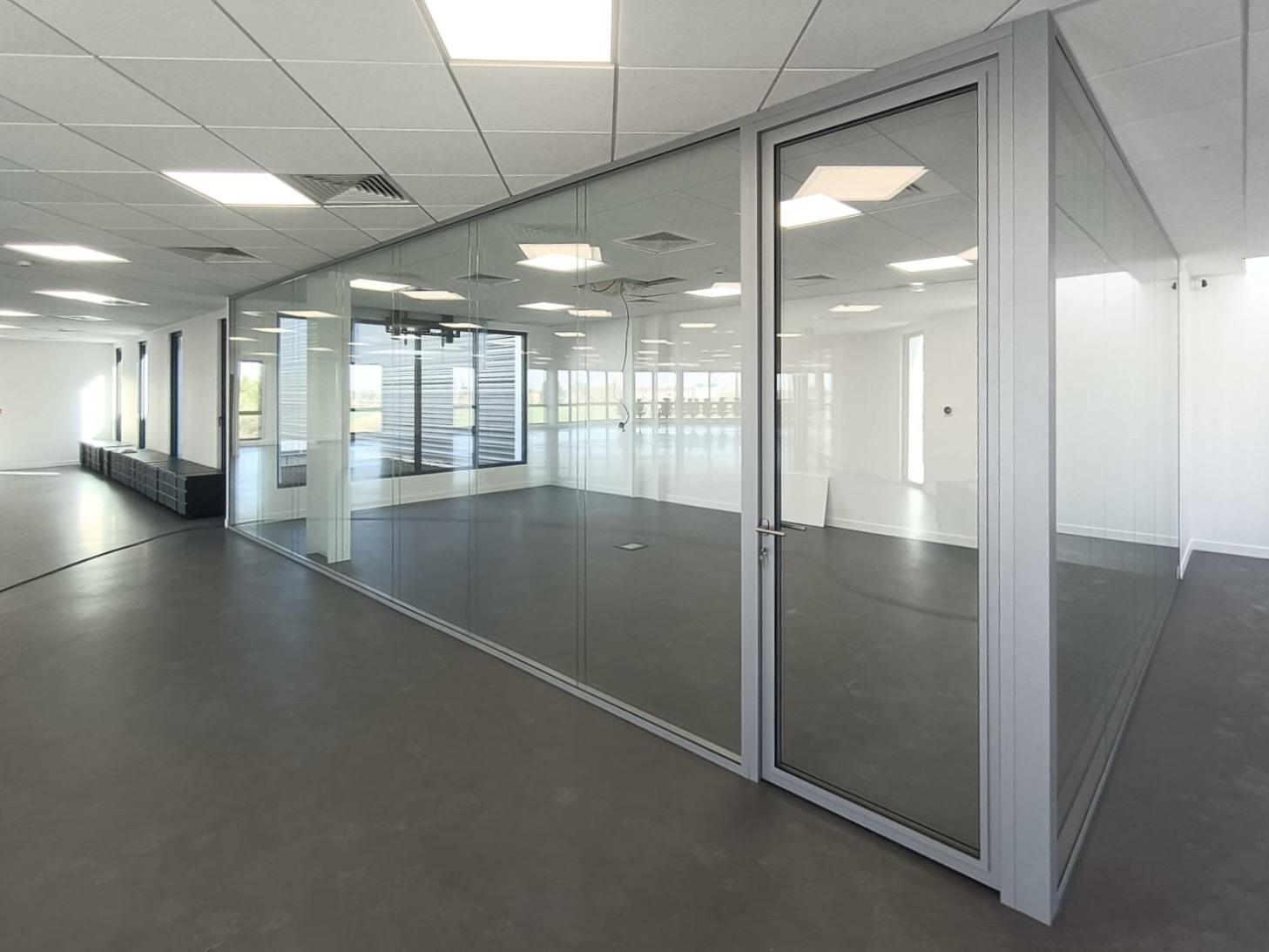 Cloisons vitrées toute hauteur à ossature grise et porte vitrée dans un plateau de bureaux