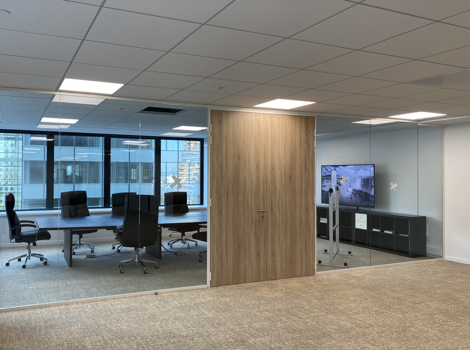Salle de réunion délimitée par des cloisons vitrées bord à bord avec une porte toute hauteur finition bois