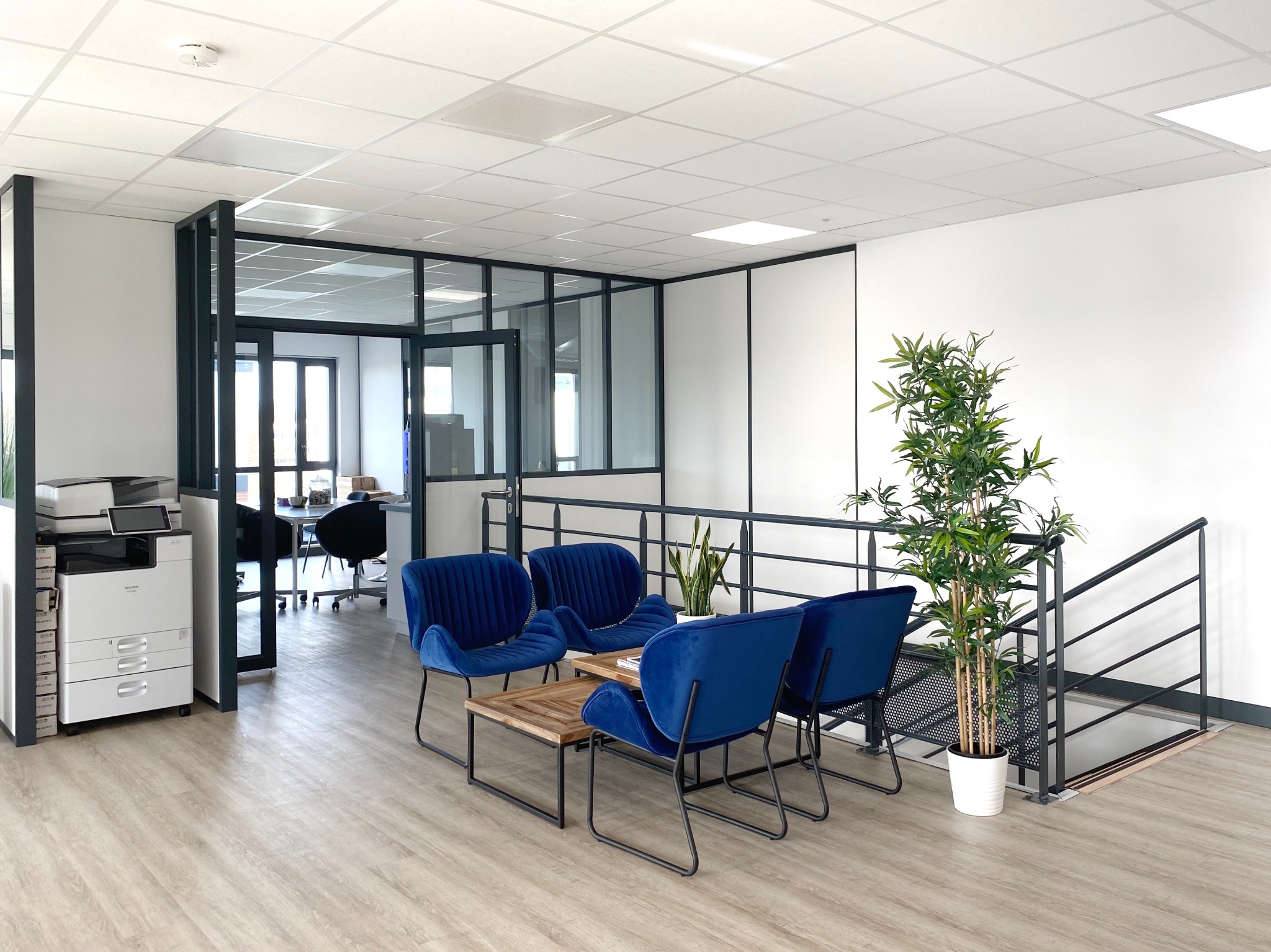 Espace d’accueil avec fauteuils bleus et cloisons vitrées sur la mezzanine